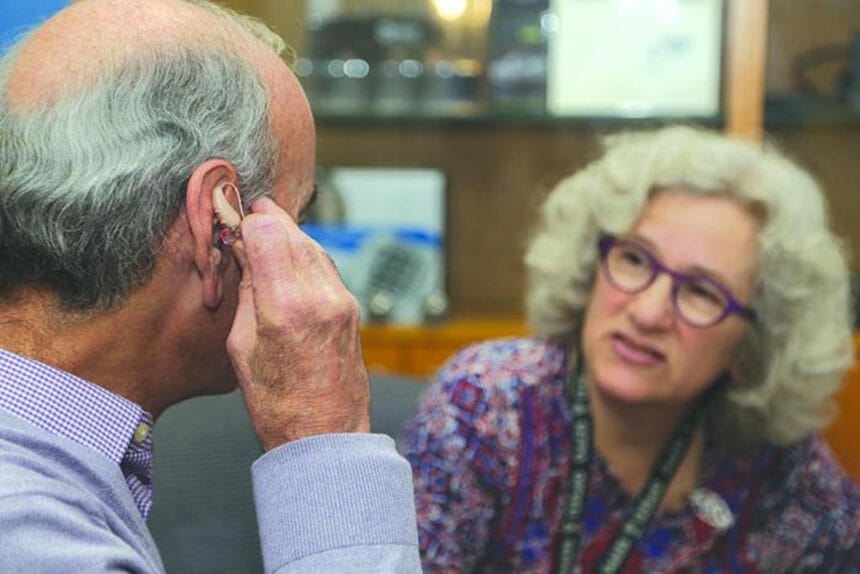An older adult tries on a hearing aid as a woman looks on.