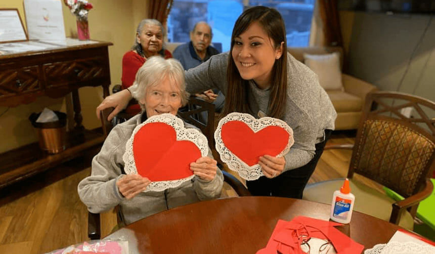 An older woman and worker pose with Valentines that they are making.