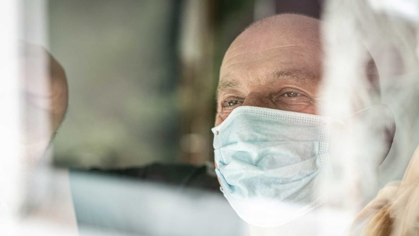 man with face mask looking out window