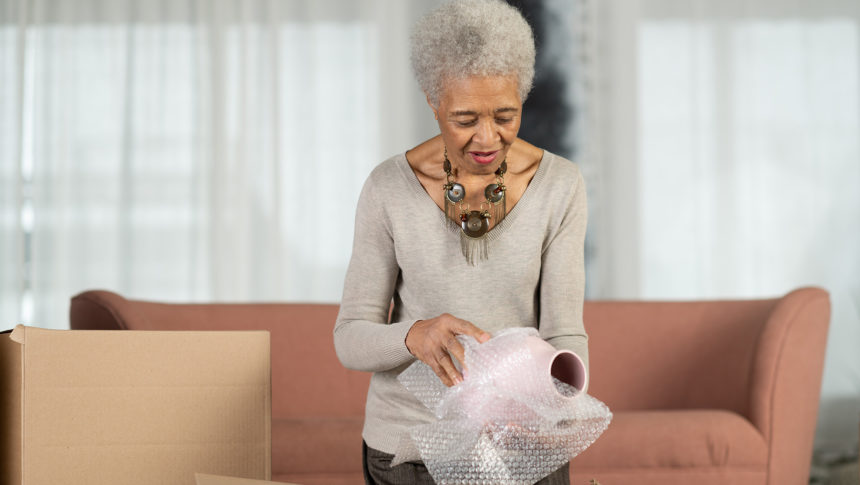 older woman wrapping a vase in bubble wrap