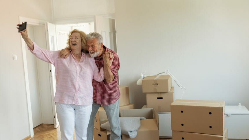 older couple taking selfie in new place, with moving boxes