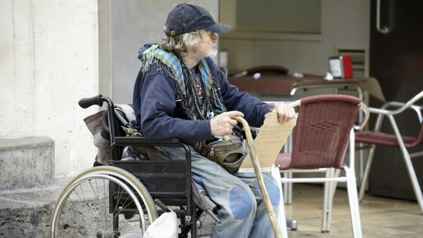 Eldery male beggar sat in wheelchair begging for money.