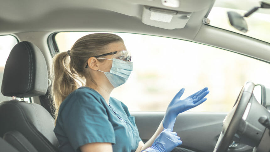 Worker in car with face mask puts on rubber glove.