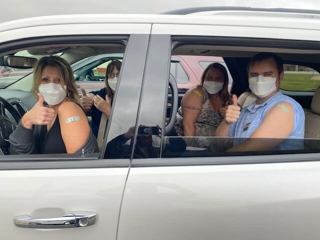 people giving thumbs up from a car after having received vaccines