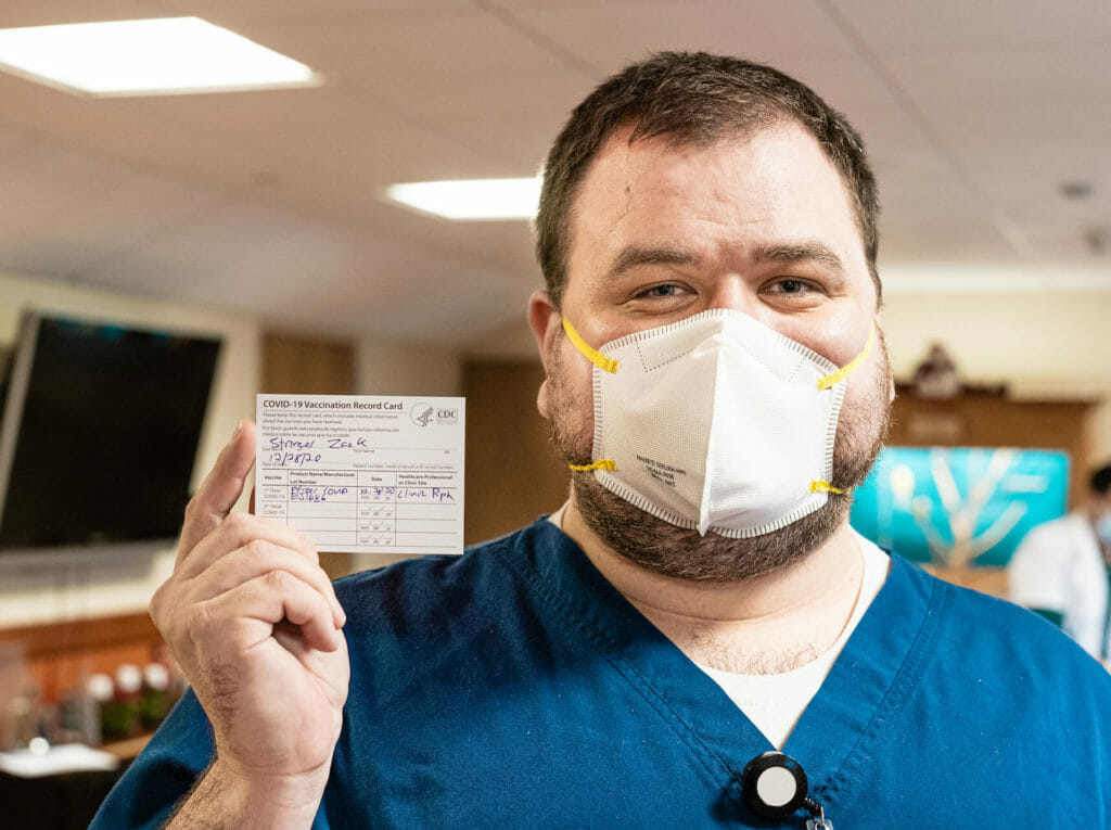 man wearing mask holding up his vaccination card