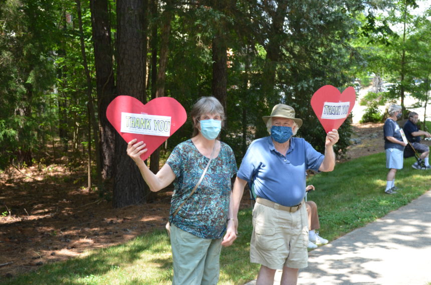 Older couple holding construction paper hearts with thank you staff messages