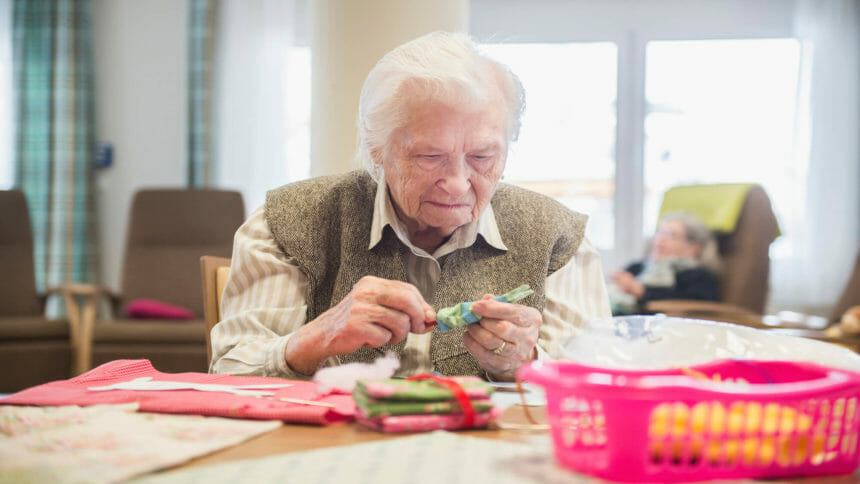 Senior sits at table at adult day services center doing a craft project
