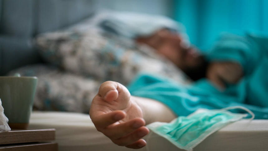 Patient lies sick in bed at home with blue blanket