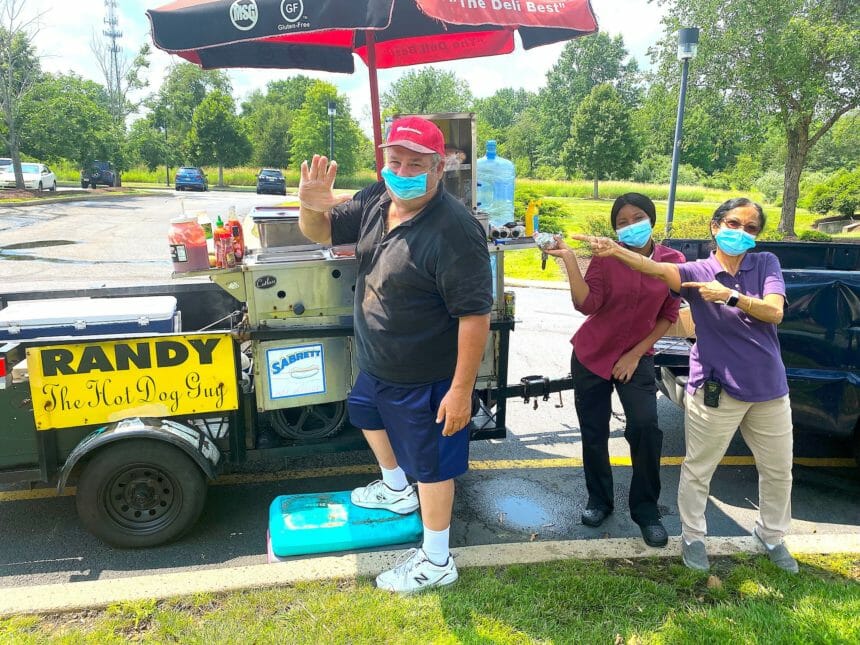 man standing at hot dog cart with two women