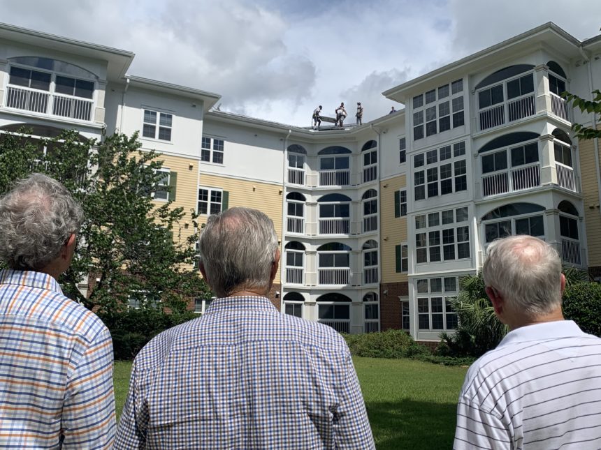 Men watching solar panels be installed on a building.