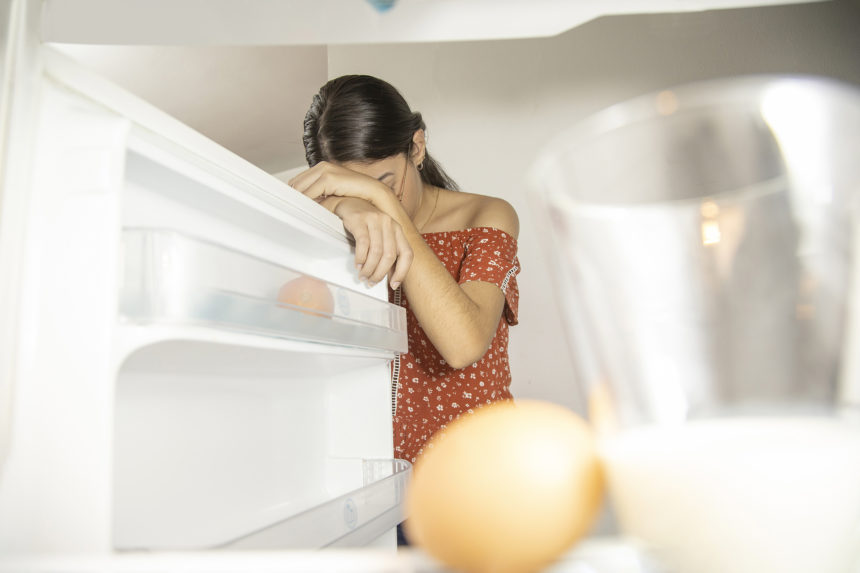 woman looking into almost empty refrigerator