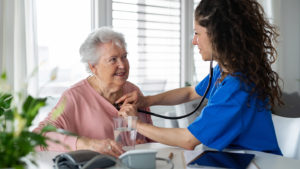 Nurse in blue scrubs checks older woman using stethoscope