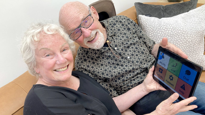 Two older adults sitting on a couch holding an iPad