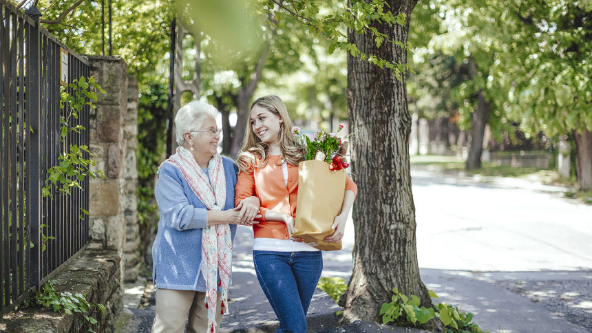 Young woman helping older woman carry groceries home