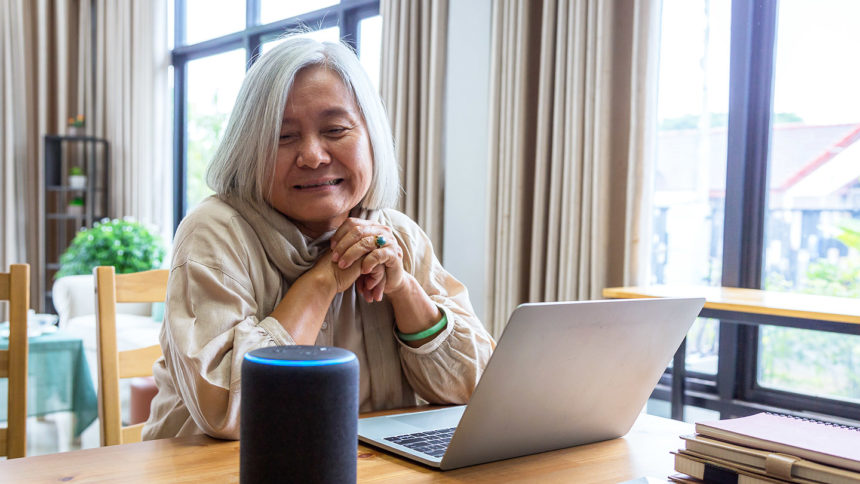 Woman in front of laptop looking at an Alexa device.