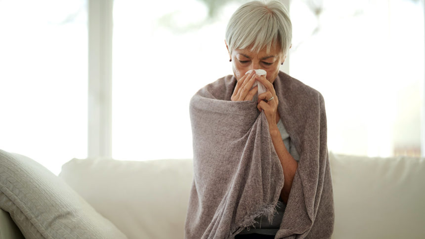 woman wrapped in blanket blowing her nose