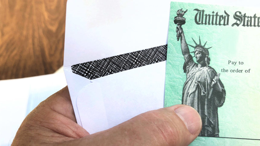 closeup of hand holding a government check and an envelope