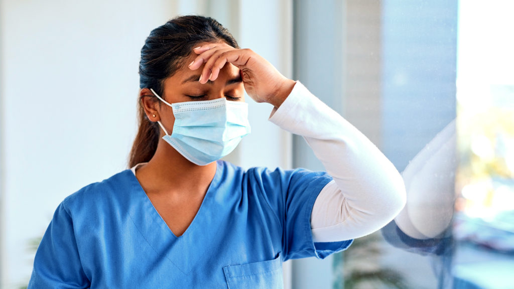 masked healthcare worker holding her head