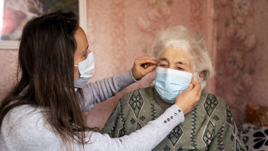 Young woman placing a mask on her grandmother