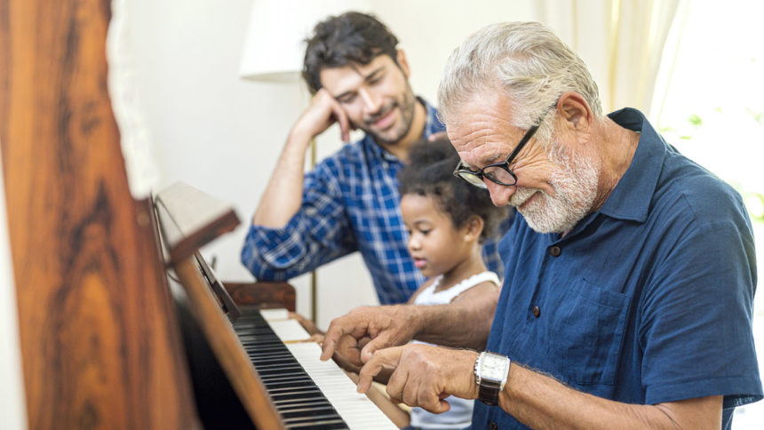 Older man plying piano with young girl and son.