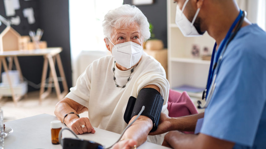 Male caregiver measuring blood pressure of senior woman.