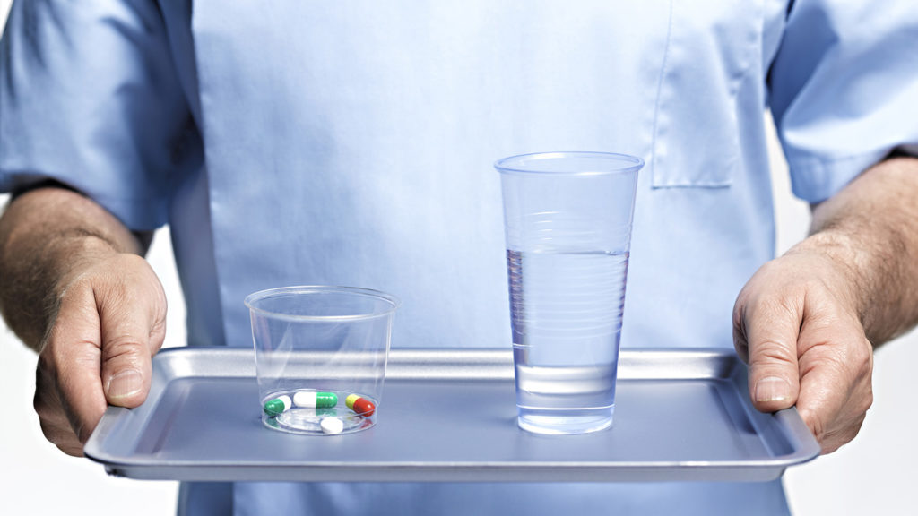 Closeup of nurse bringing medication and glass of water on a tray