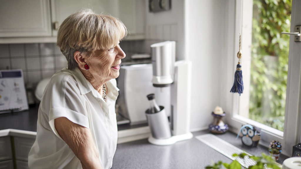 Smiling senior woman in kitchen at home looking out of window