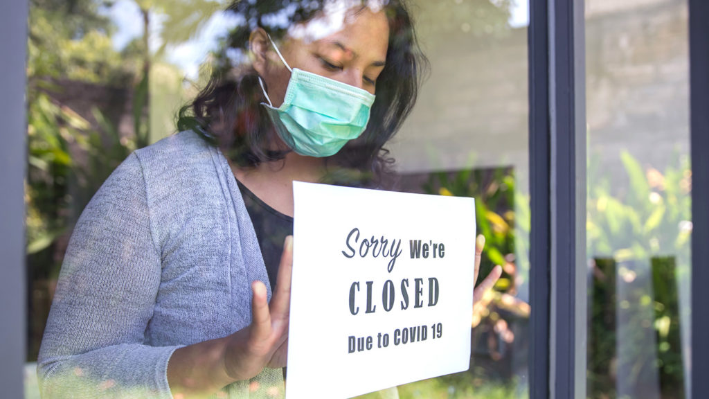 Woman posting closed sign in business window due to Covid