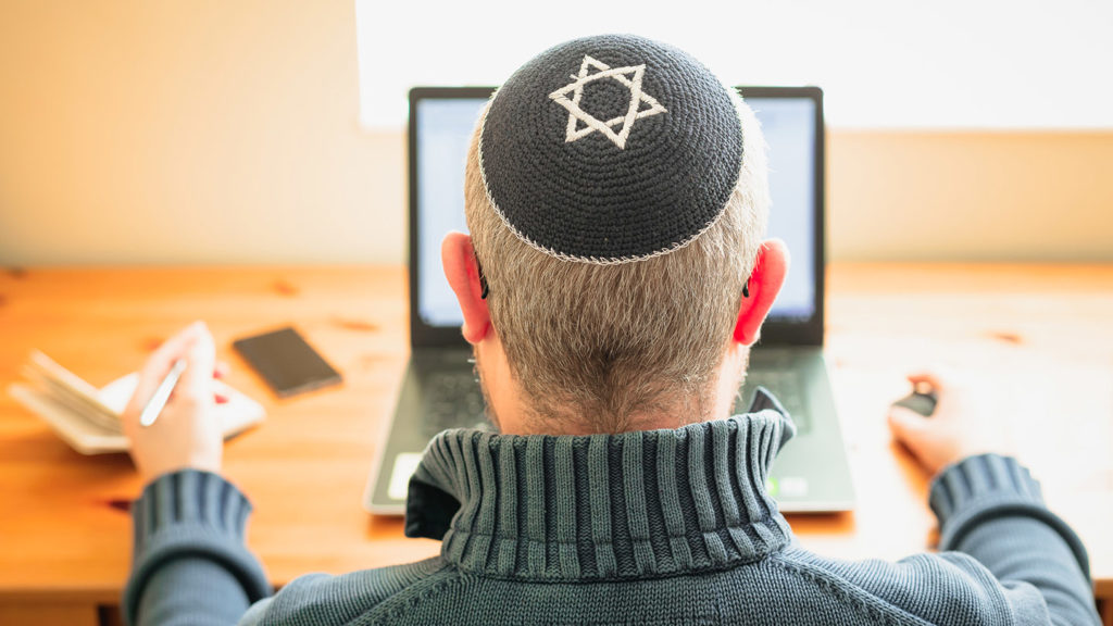 Jewish man wearing skull cap working from home