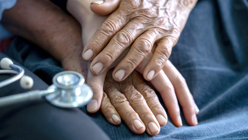 Close up of young nurse holding old man's hands and encourage him.