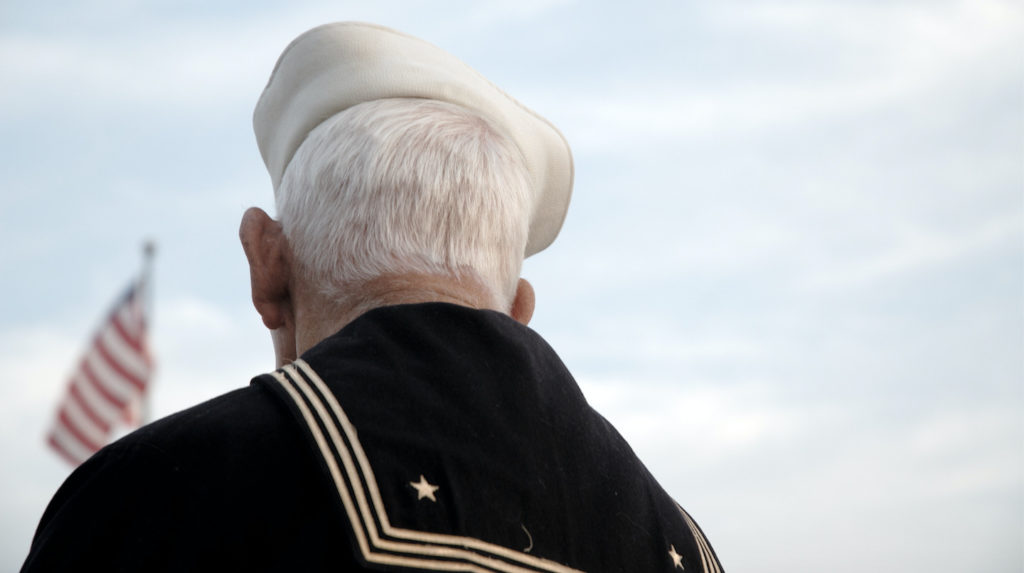 Older man in Navy suite looking at flag