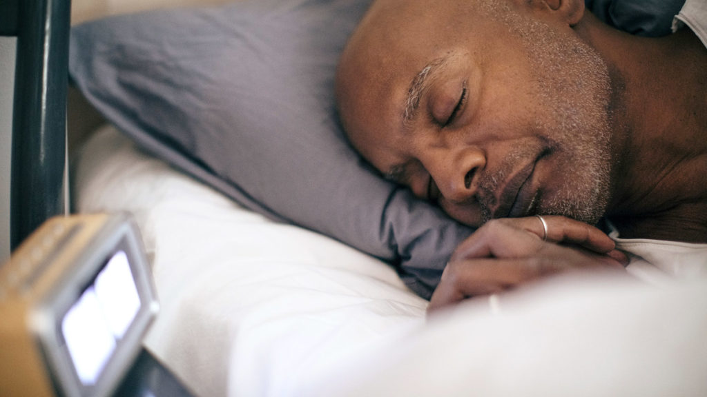 Retired senior man sleeping on bed by alarm clock at home