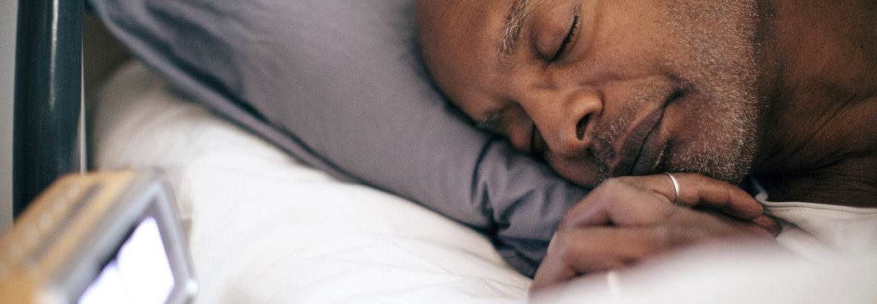 Retired senior man sleeping on bed by alarm clock at home