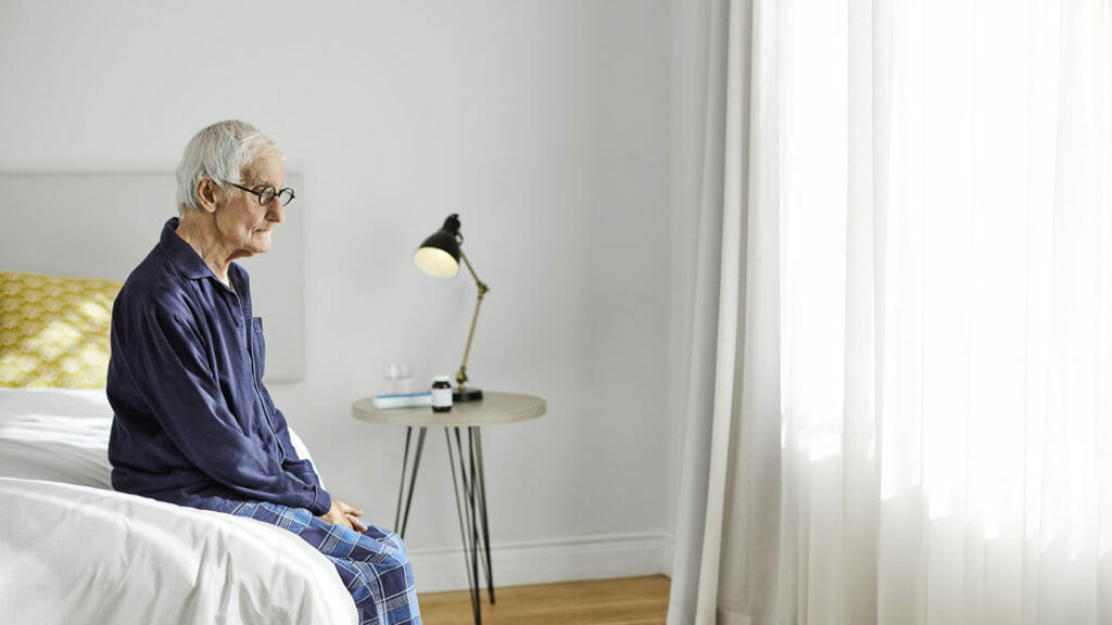 Thoughtful senior man sitting on bed. Elderly male is looking away. He is in bedroom at home.