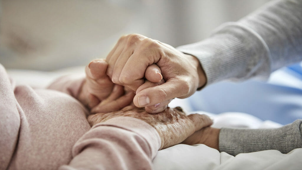Middle section of an elderly woman holding a nurse's hand.  The caregiver supports the elderly.  They are at home during the coronavirus lockdown.