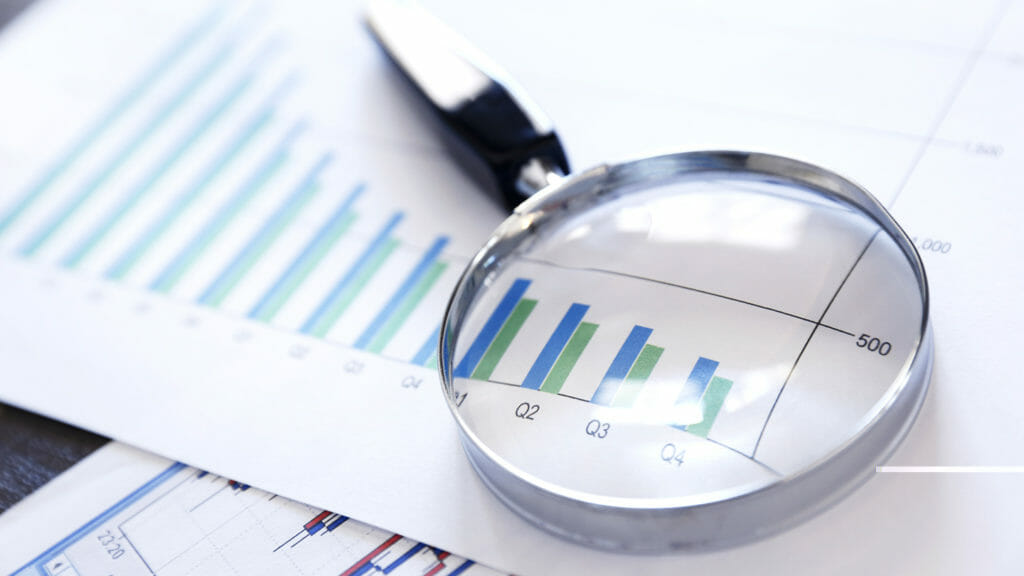 A magnifying glass rests on top of a bar graph that shows declining sales or performance over a quarterly basis. The image is photographed using a very shallow depth of field.