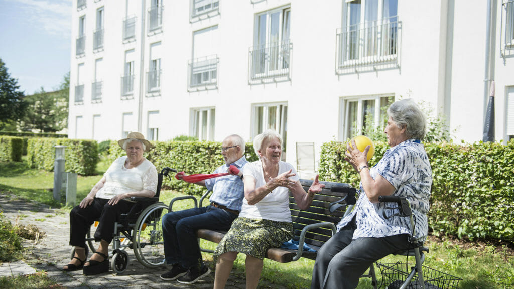 Image of senior women and man exercising with resistance band at assisted living garden