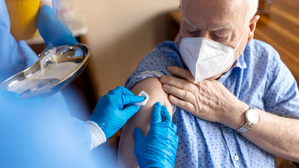 Senior man getting coronavirus vaccine at home by a healthcare worker. Healthcare worker disinfecting arm of a senior man before giving a vaccine at home.