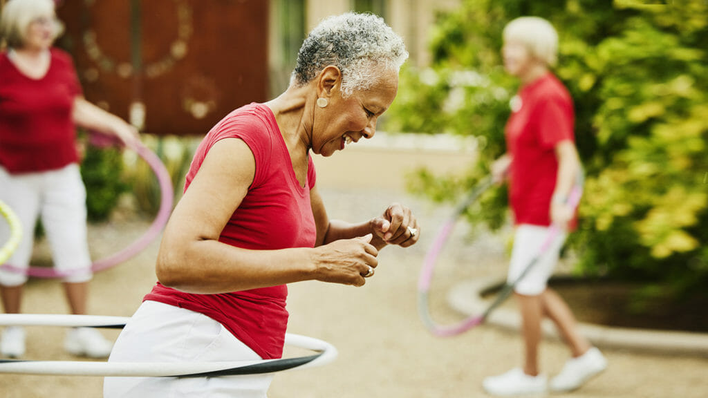 Medium shot of smiling senior woman exercising with spinning plastic hoops in backyard