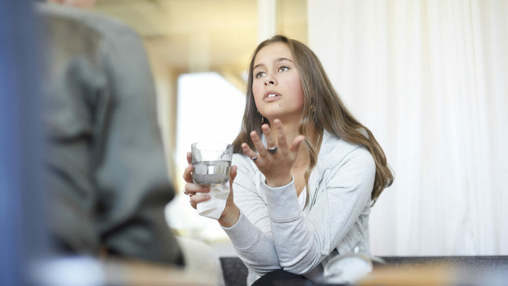 Depressed teenager talking to therapist while drinking water at workshop