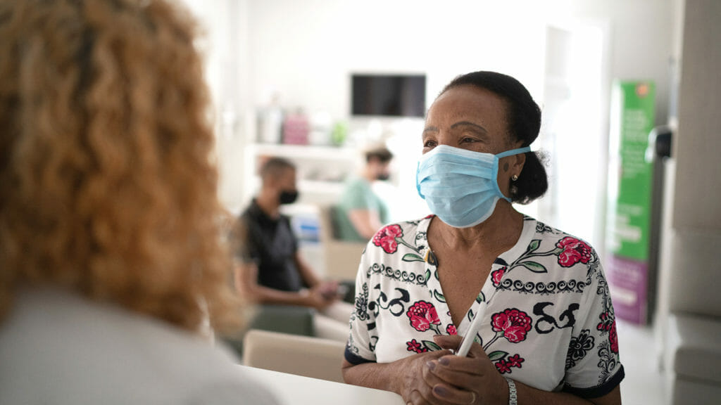 Medical clinic reception, patient waiting in line respecting social distancing using face mask