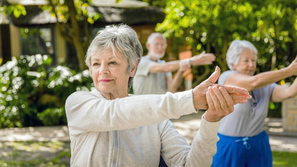 Active senior woman with friends exercising in yard