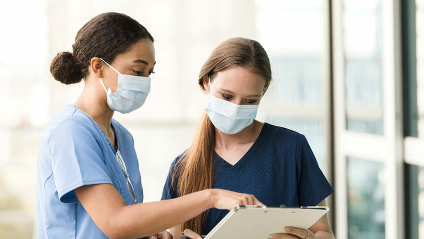 Two female surgeons wear their protective masks to prevent the spread of COVID-19 as they discuss a patient chart.