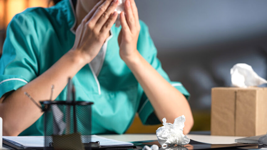 cropped view of nurse in uniform sneezing and holding napkin during night shift