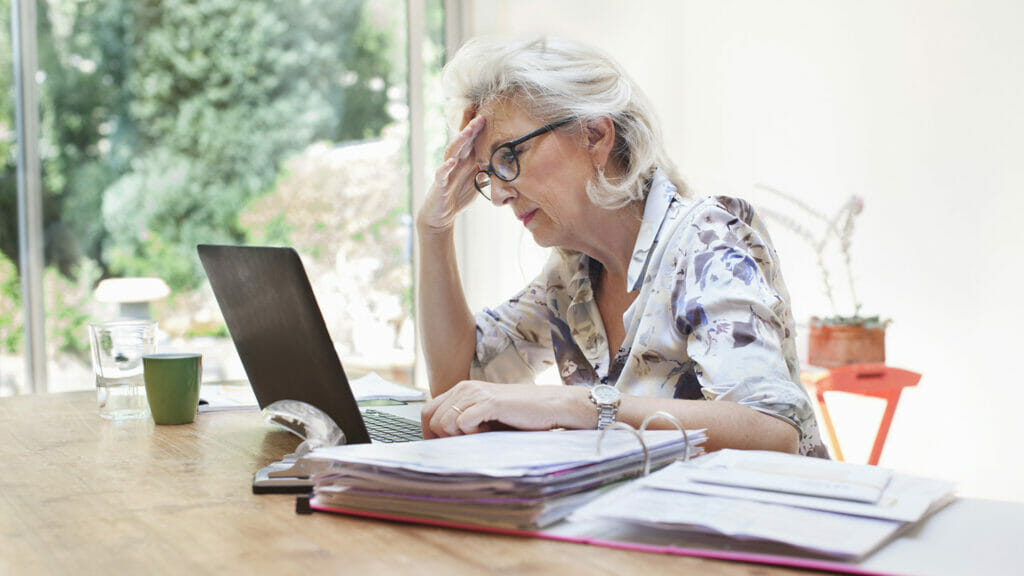 Senior woman sitting at table, using laptop, worried expression