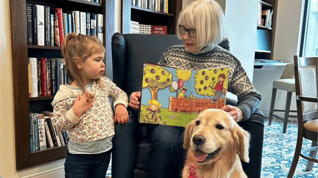 Older woman reading to a child while a dog looks on
