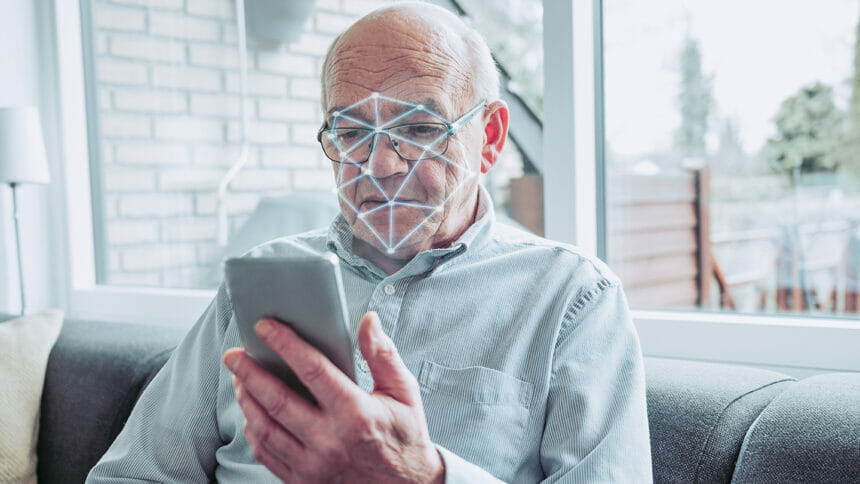 Senior man holds smart phone and it performs a scan of his face. Facial recognition software on the phone can unlock the screen and even pay for items online.