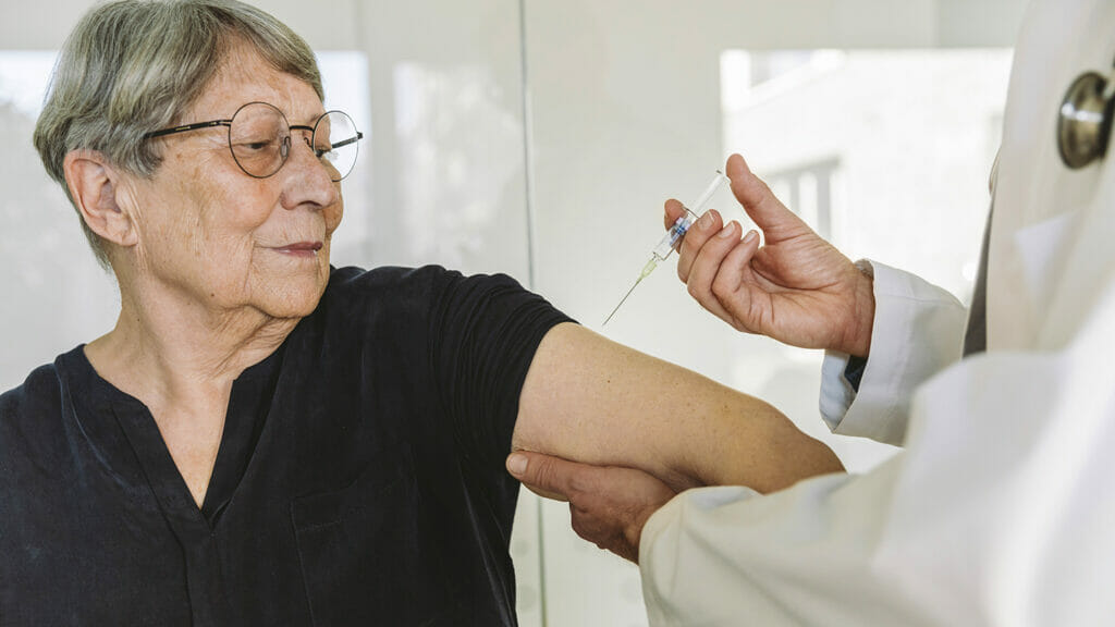 Doctor injecting vaccine into senior patient’s arm, Cologne, NRW, Germany