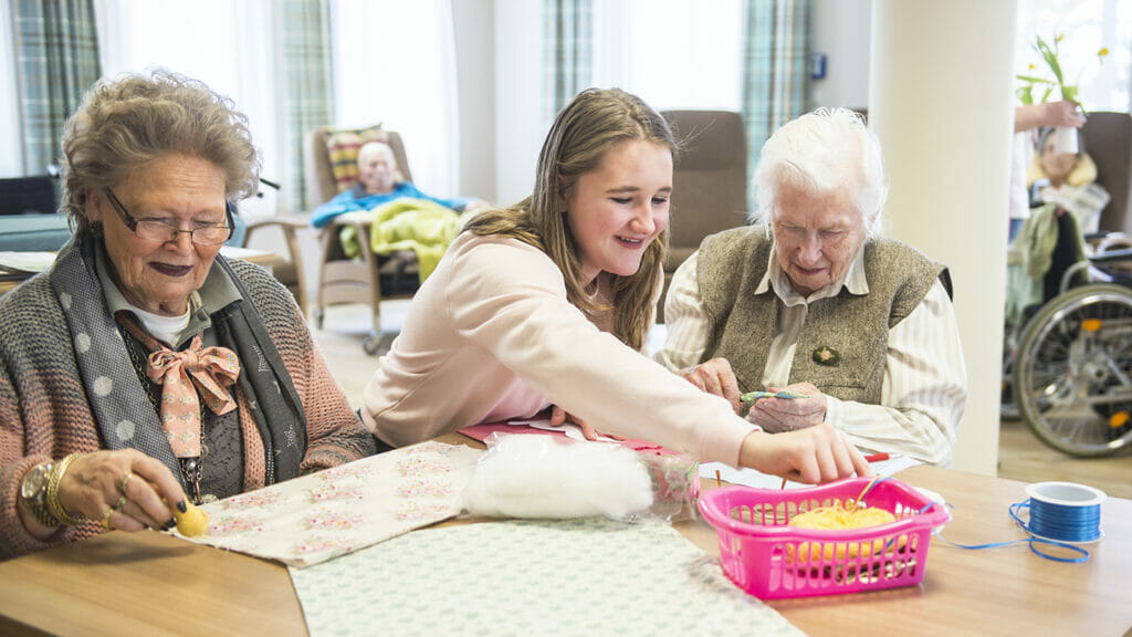 Senior women with girl doing craft activity at rest home