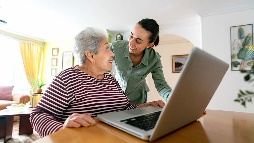 Young Latin American woman helping a senior woman paying her bills online on her laptop - lifestyle concepts